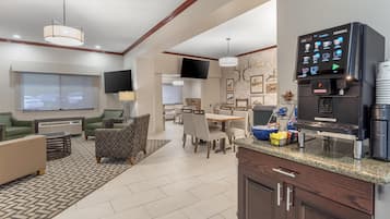 A modern hotel room with a kitchenette, dining area, and a large TV screen.