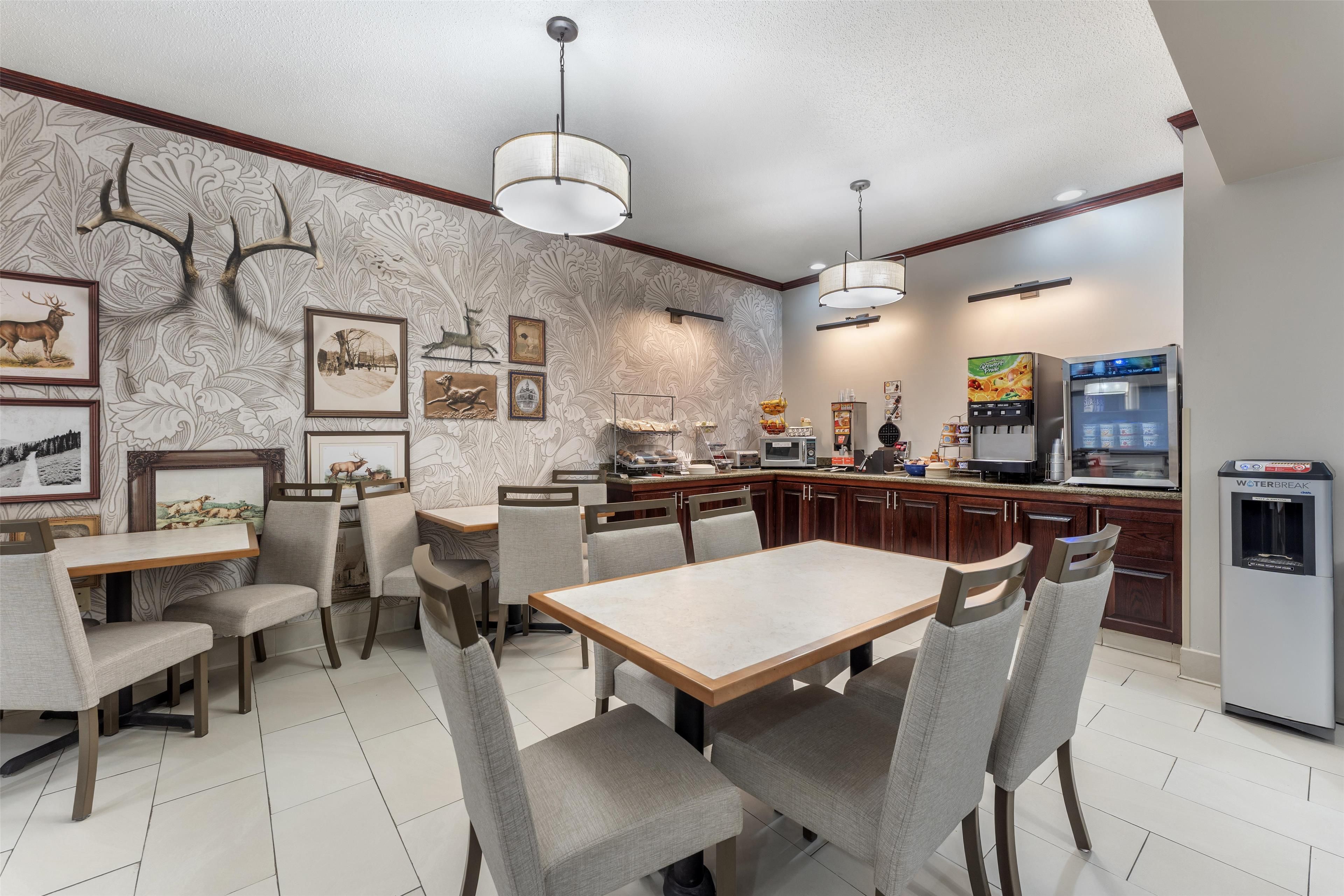 A dining area with a large table and chairs, a kitchen with a refrigerator and microwave, and wall-mounted artwork.