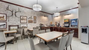 A dining area with a large table and chairs, a kitchen with a refrigerator and microwave, and wall-mounted artwork.