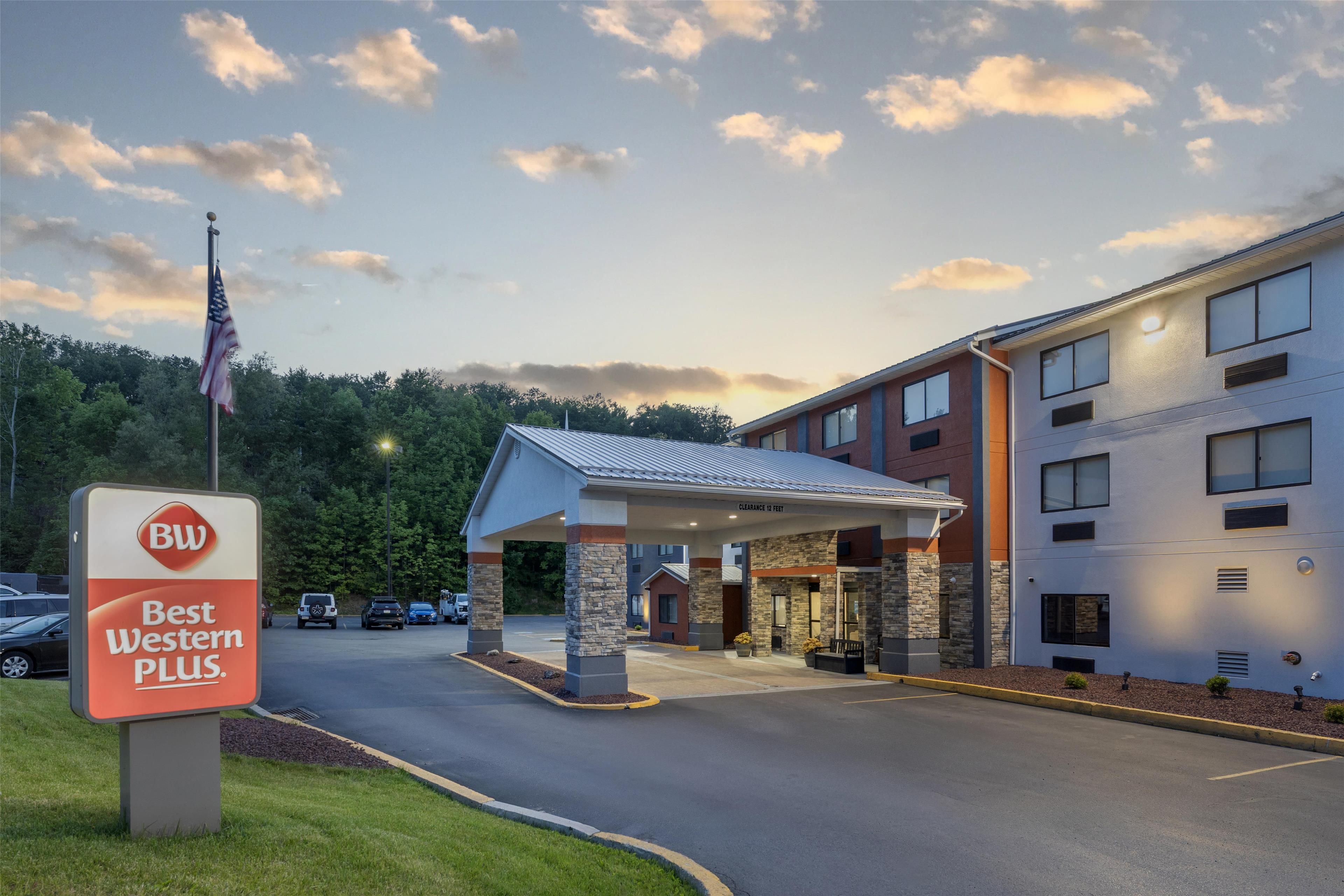 A Best Western Plus hotel with a covered entrance, a parking lot, and a flagpole with an American flag.