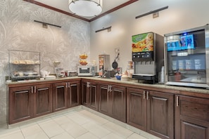 A modern kitchen with dark wood cabinets, a granite countertop, a microwave, a coffee machine, and a beverage dispenser. - Best Western Plus Executive Inn (St. Marys)