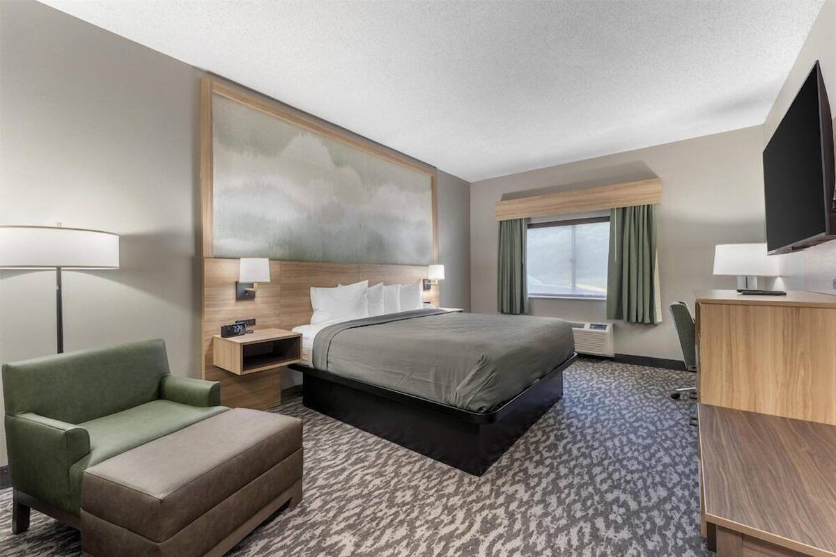A hotel room with a bed, a desk, a chair, a TV, and a painting on the wall.