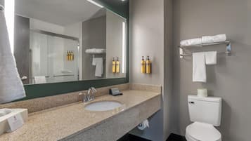 A modern bathroom with a granite countertop sink, a large mirror, a toilet with a towel rack, and two bottles of toiletries on the wall.