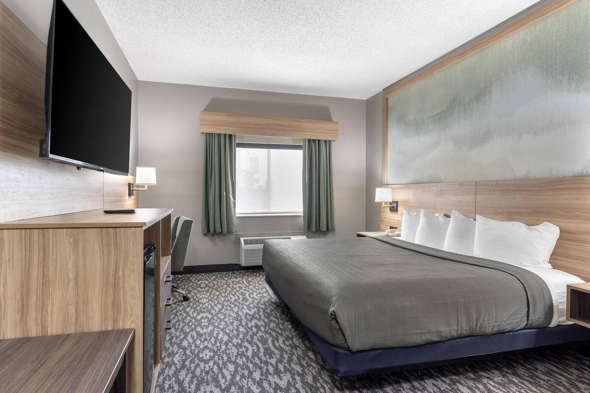 A hotel room with a bed, a desk, a television, and a window with curtains.
