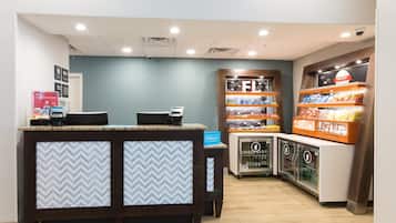 Zona de recepción de un hotel con mostrador, minibar y exhibición de snacks.