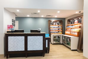A hotel reception area with a counter, a minibar, and a snack display. - Hampton Inn St. Augustine Beach (St. Augustine)