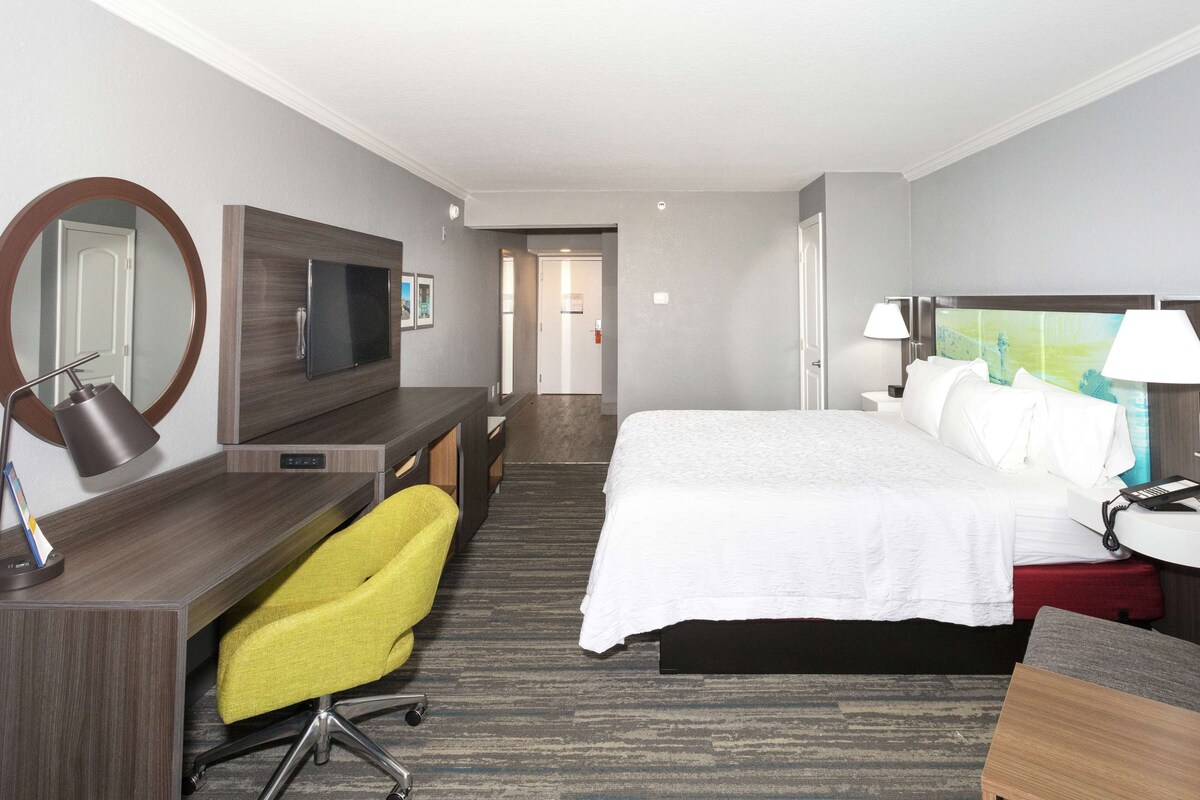 A hotel room with a bed, desk, chair, TV, and a bathroom door.