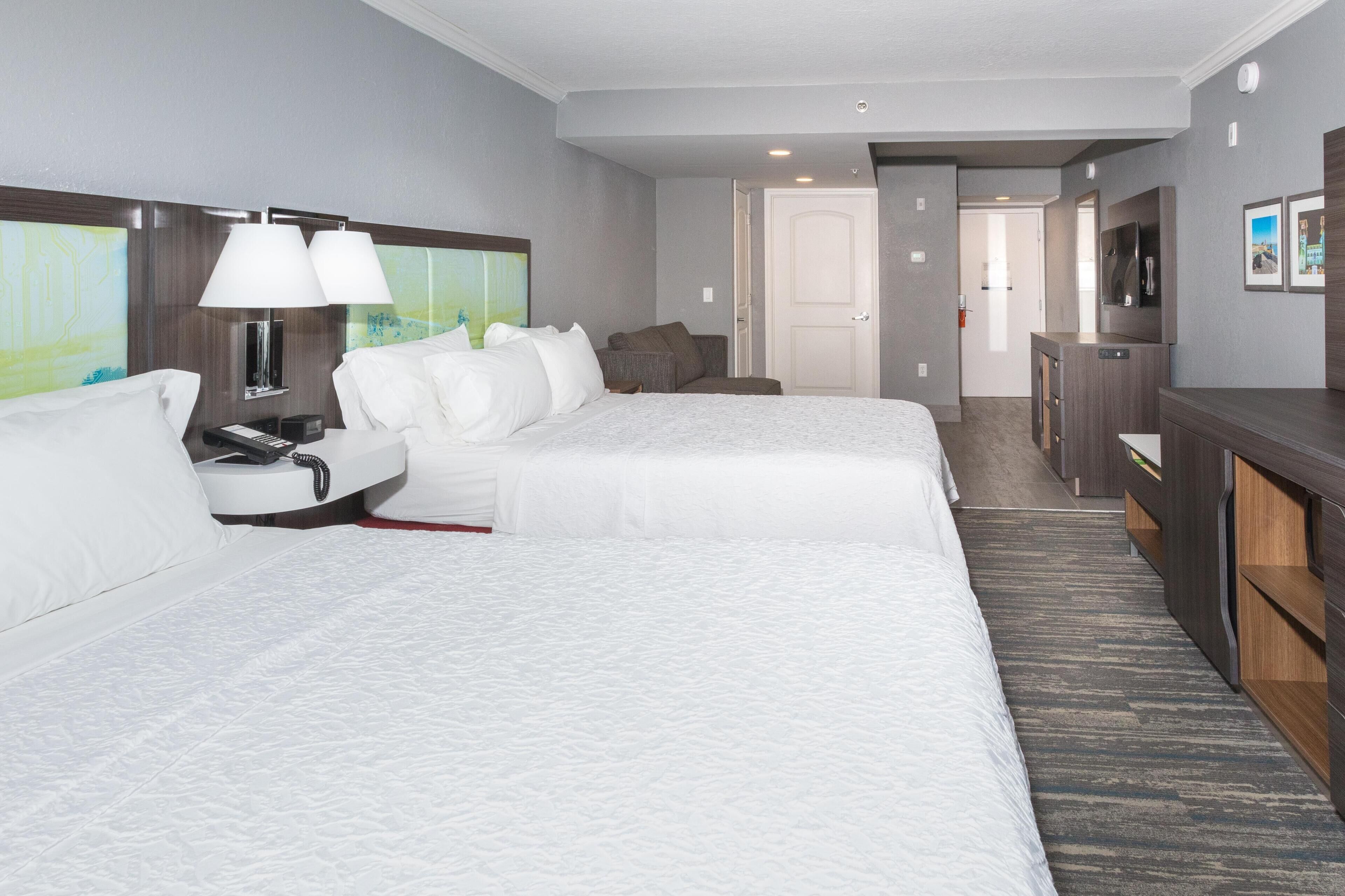 A hotel room with two beds, a desk, a chair, a TV, and a painting on the wall.
