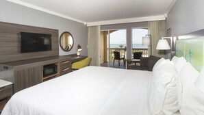 A hotel room with a large bed, a desk, a TV, a mirror, and a balcony with a view of the sea. - Hampton Inn St. Augustine Beach (St. Augustine)