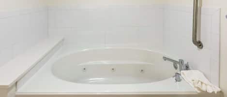 A white bathtub with a grab bar, a towel, and a shelf.
