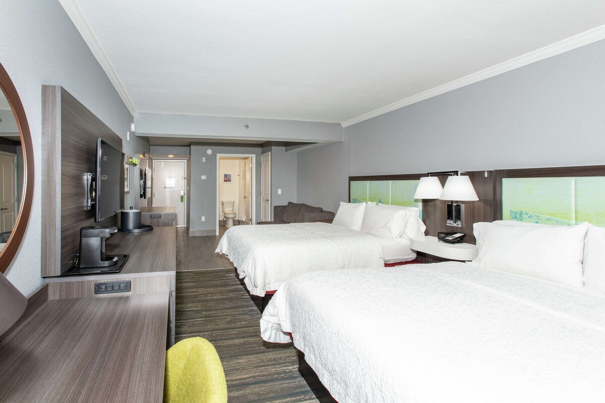 A hotel room with two beds, a desk with a computer, a TV, and a large mirror.