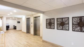 Un vestíbulo de hotel con suelo de madera, un ascensor y tres paneles decorativos en la pared.