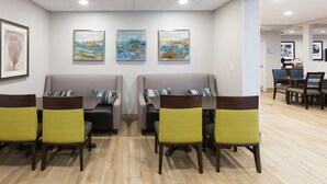 A waiting area with two sofas and four chairs, a wooden floor, and three framed artworks on the wall. - Hampton Inn St. Augustine Beach (St. Augustine)