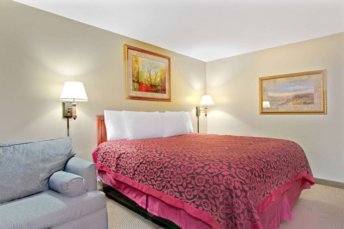 A hotel room with a bed, two bedside lamps, a chair, and two framed pictures on the walls.