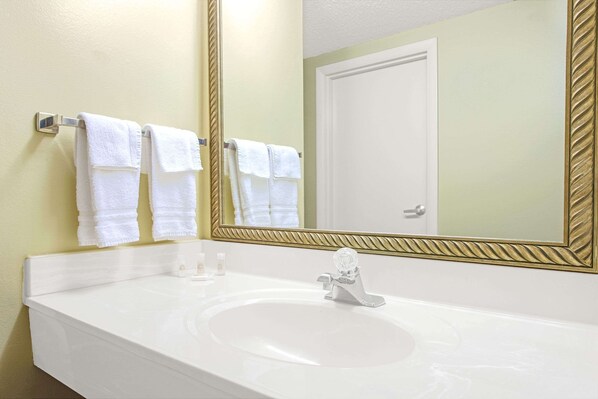 A bathroom with a white sink, a mirror with a gold frame, and three white towels hanging on a towel rack.