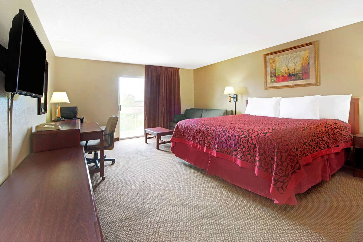 A hotel room with a bed, desk, chair, television, and a painting on the wall.