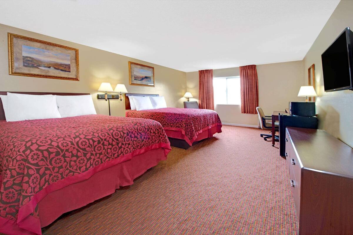 A hotel room with two beds, a desk, a TV, and two lamps.