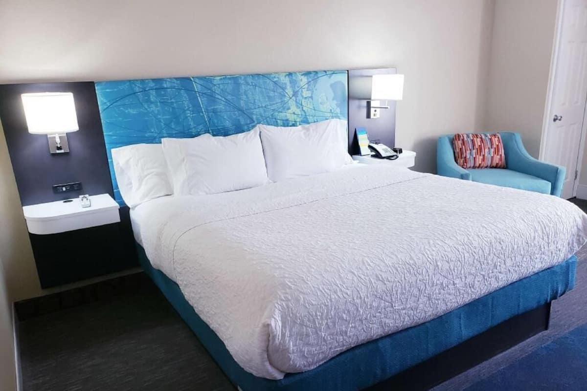 Ein Hotelzimmer mit einem großen Bett, zwei Nachttischen, einem Sessel und einem Beistelltisch mit einer Lampe.
