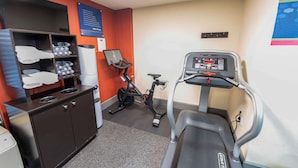 Une salle de sport équipée d’un tapis de course, d’un vélo d’appartement et d’un meuble contenant des serviettes et des bouteilles d’eau.