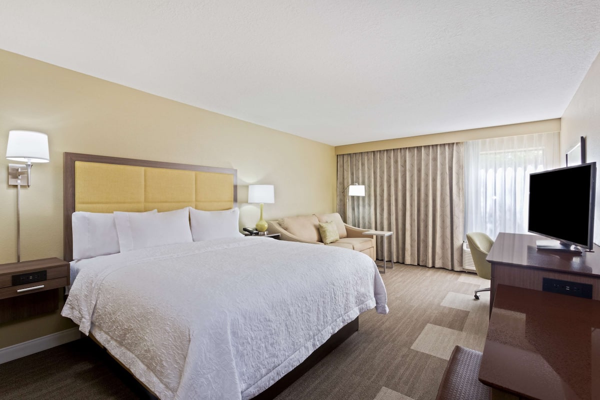 A hotel room with a large bed, bedside tables, a desk with a television, and a chair.