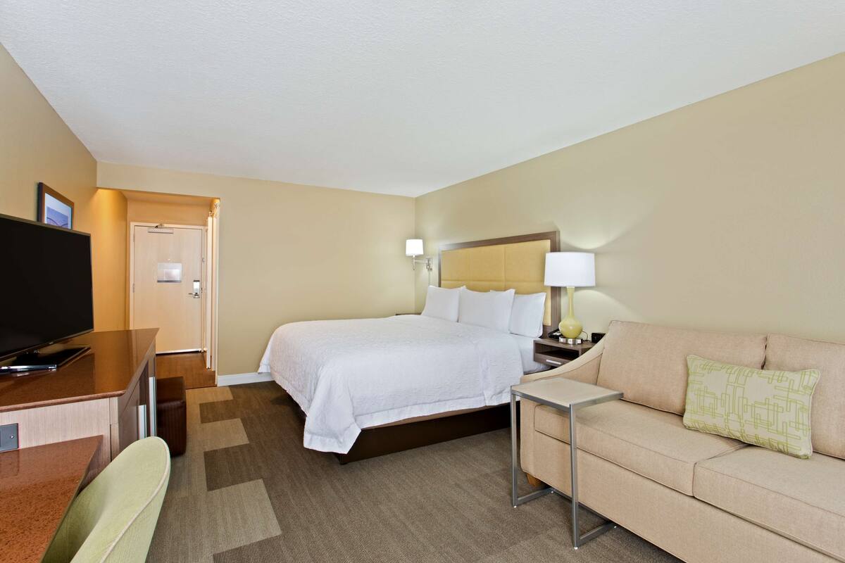 A hotel room with a bed, a television, a desk, a chair, a sofa, and a lamp.