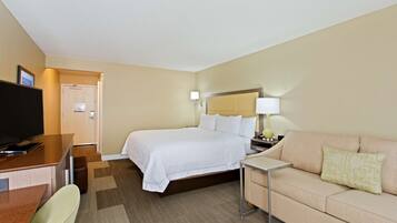 A hotel room with a bed, a television, a desk, a chair, a sofa, and a lamp.