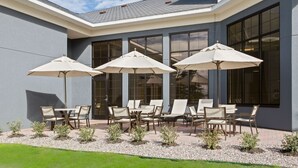 An outdoor patio with multiple tables and chairs, large umbrellas, and a view of the building's exterior. - Hampton Inn Sault Ste Marie (Sault Ste. Marie)