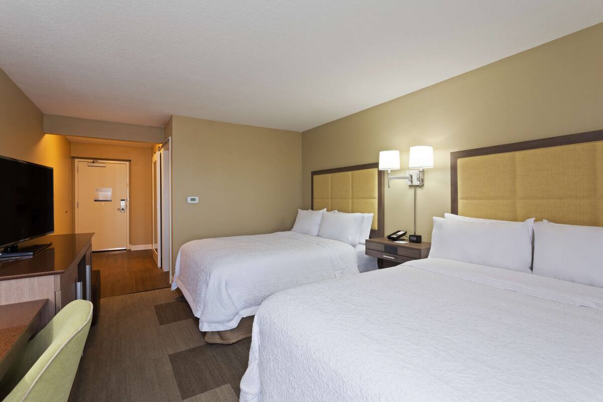 A hotel room with two beds, a TV, a desk, and a mirror.