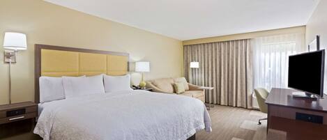 A hotel room with a large bed, a desk, a chair, and a television.