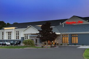 A Hampton Inn hotel with a stone facade, large windows, and a well-maintained lawn.
