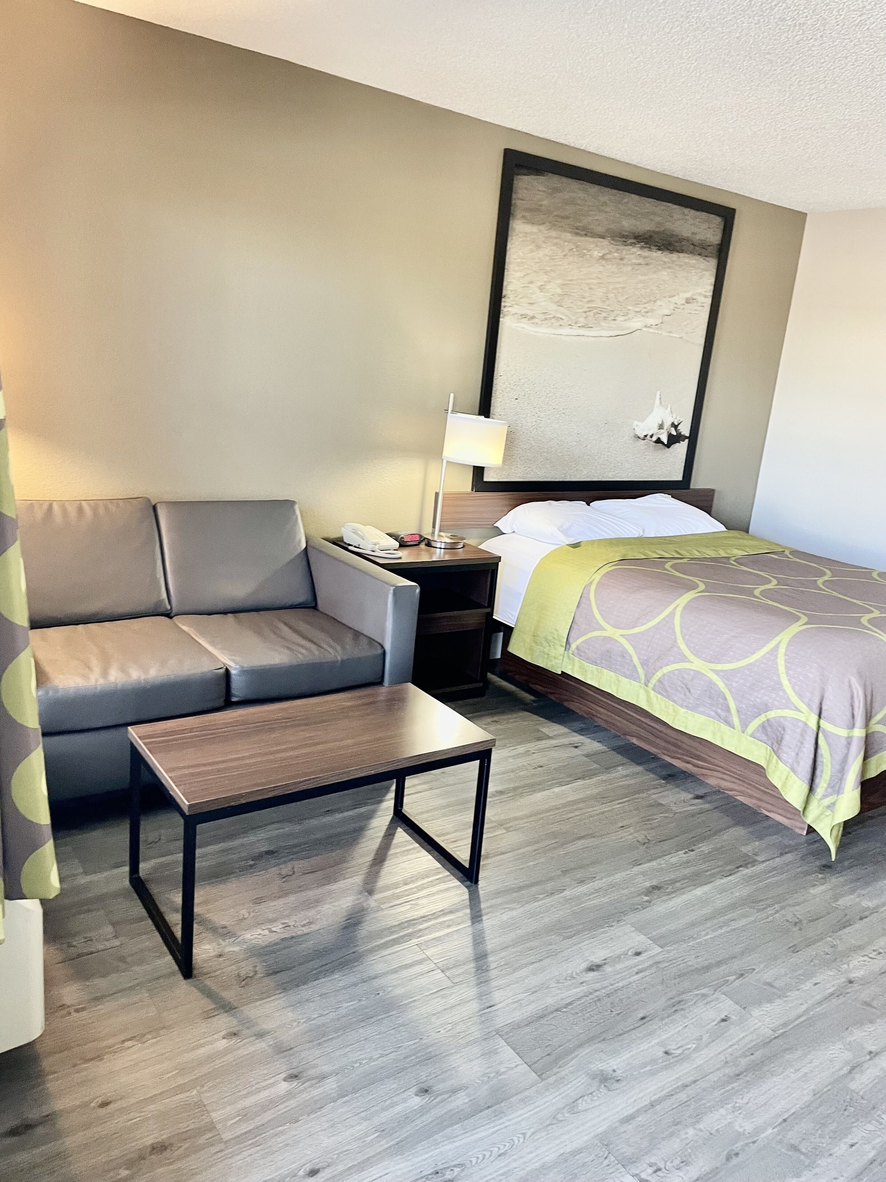 A hotel room with a bed, a sofa, a small table, a nightstand, and a lamp.