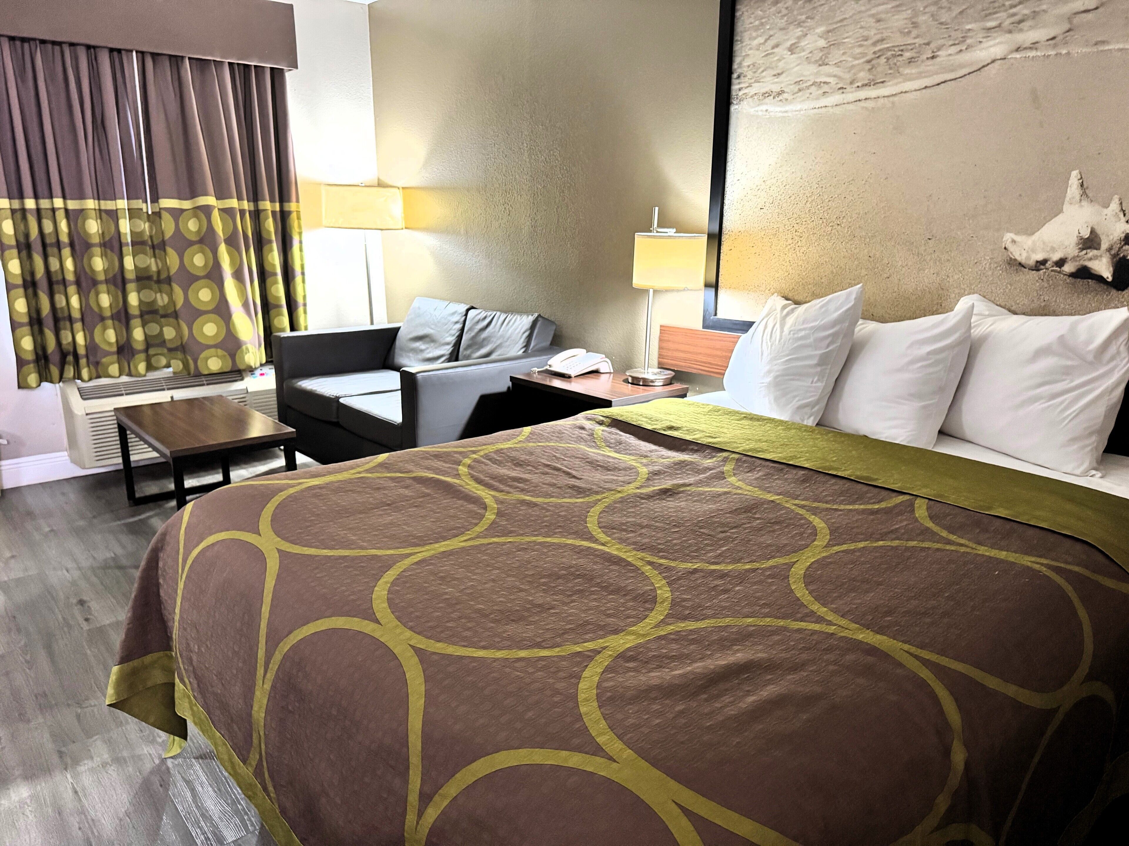 A hotel room with a large bed, a sofa, a small table, a lamp, and a nightstand.