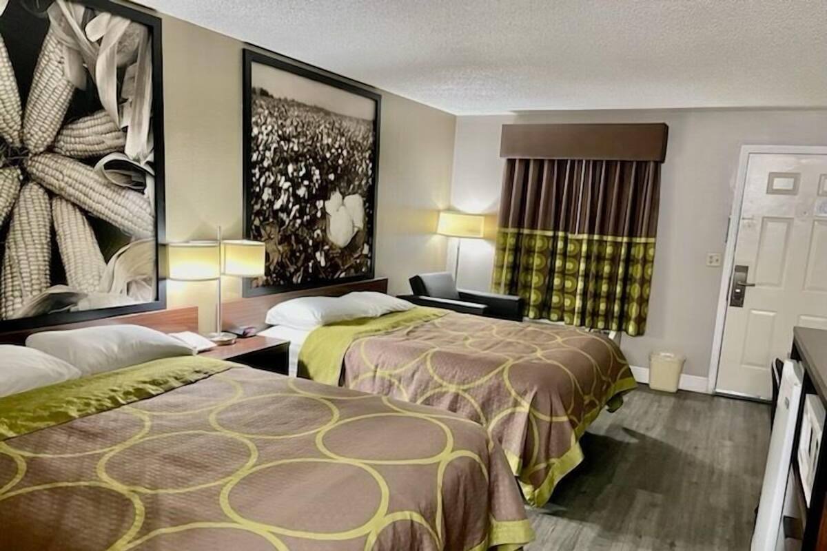 Une chambre d’hôtel avec deux lits, une grande peinture abstraite, un bureau avec une lampe et une fenêtre avec des rideaux.