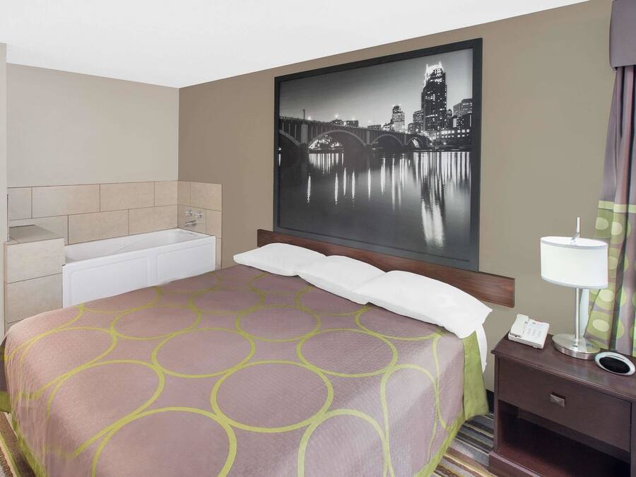 A hotel room with a bed, a nightstand, a lamp, a telephone, and a large cityscape painting on the wall.