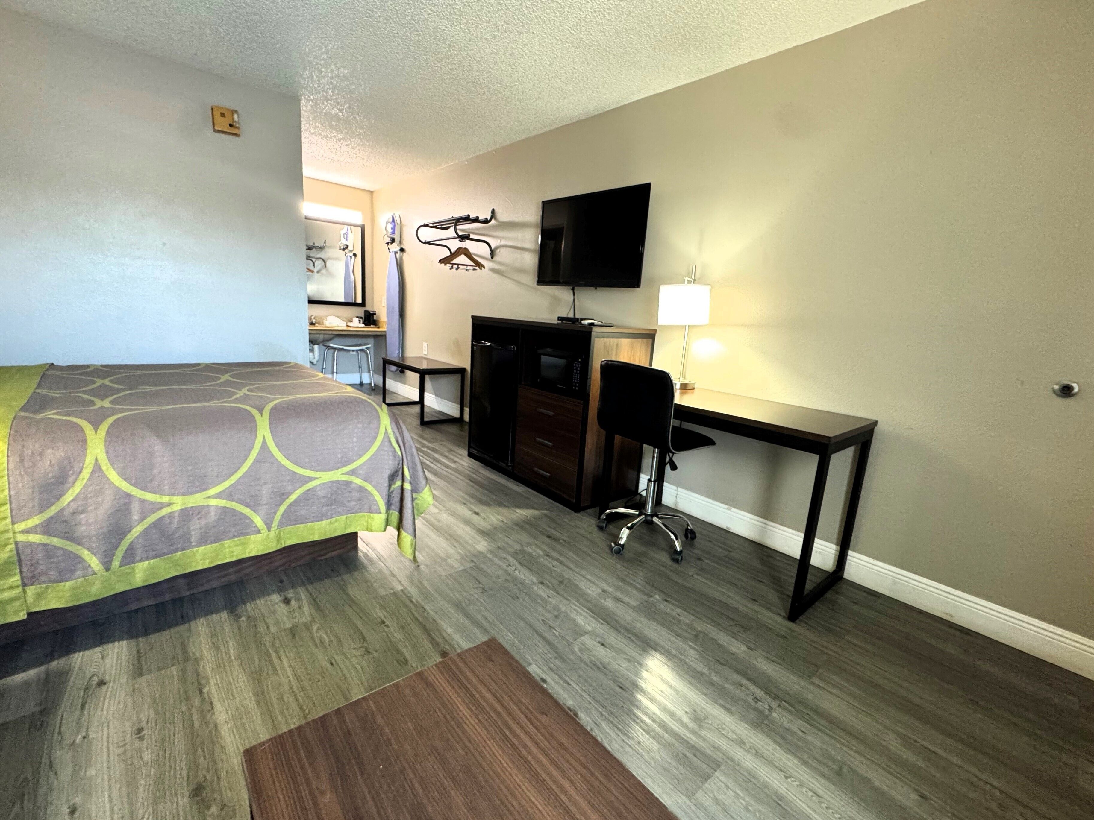 A hotel room with a bed, desk, chair, TV, and a small table.