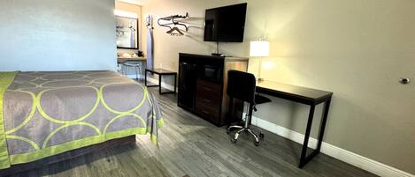 A hotel room with a bed, desk, chair, TV, and a small table.