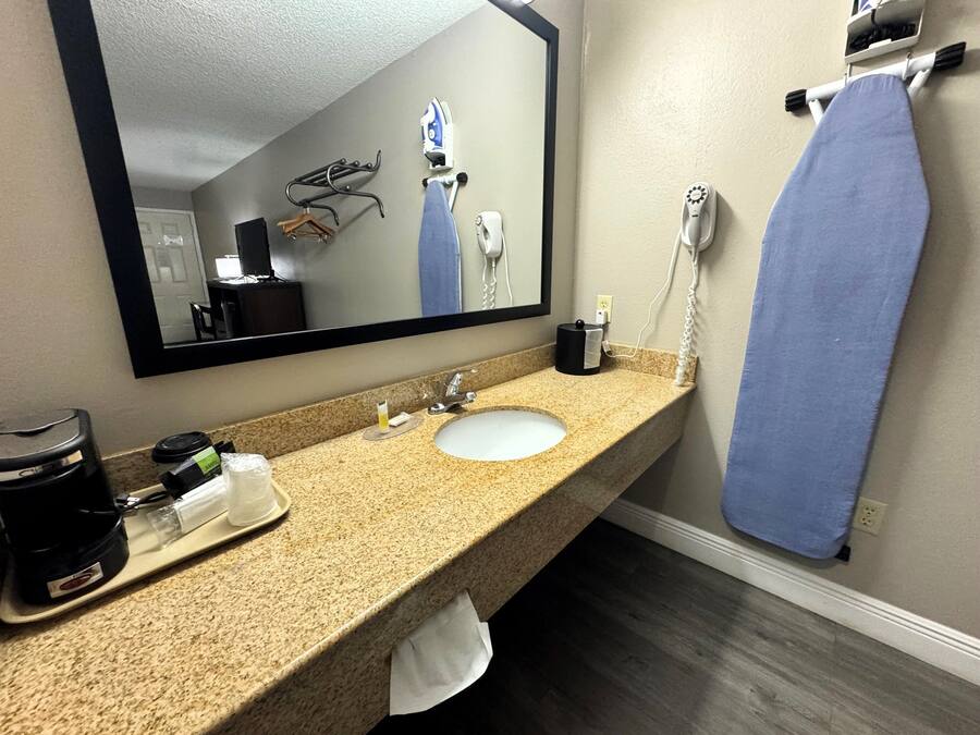 A hotel bathroom with a granite countertop, a sink, a mirror, a telephone, and a blue towel hanging on the wall.
