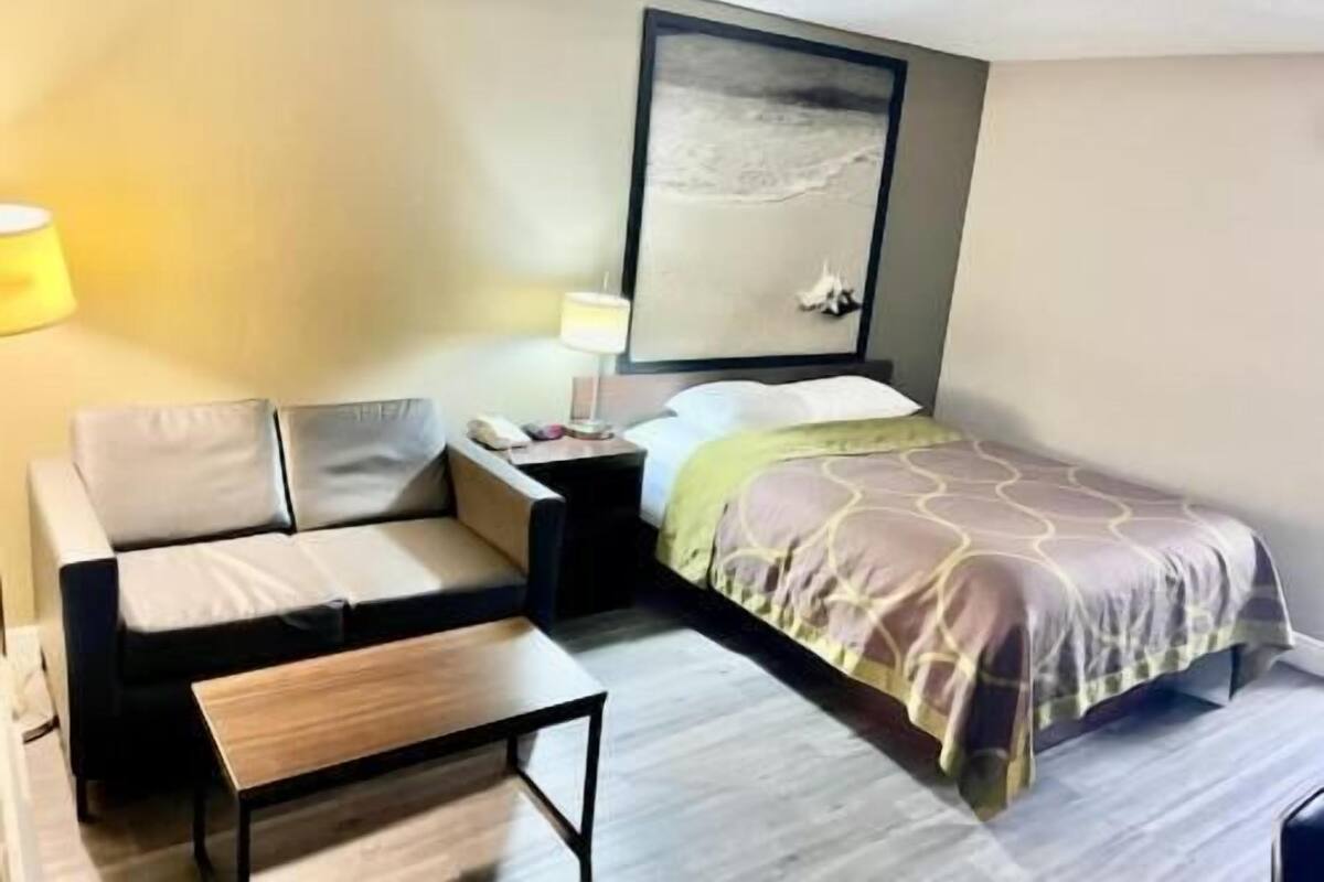 Une chambre d’hôtel comprenant un lit, un canapé, une table de chevet, une lampe et une œuvre d’art accrochée au mur.