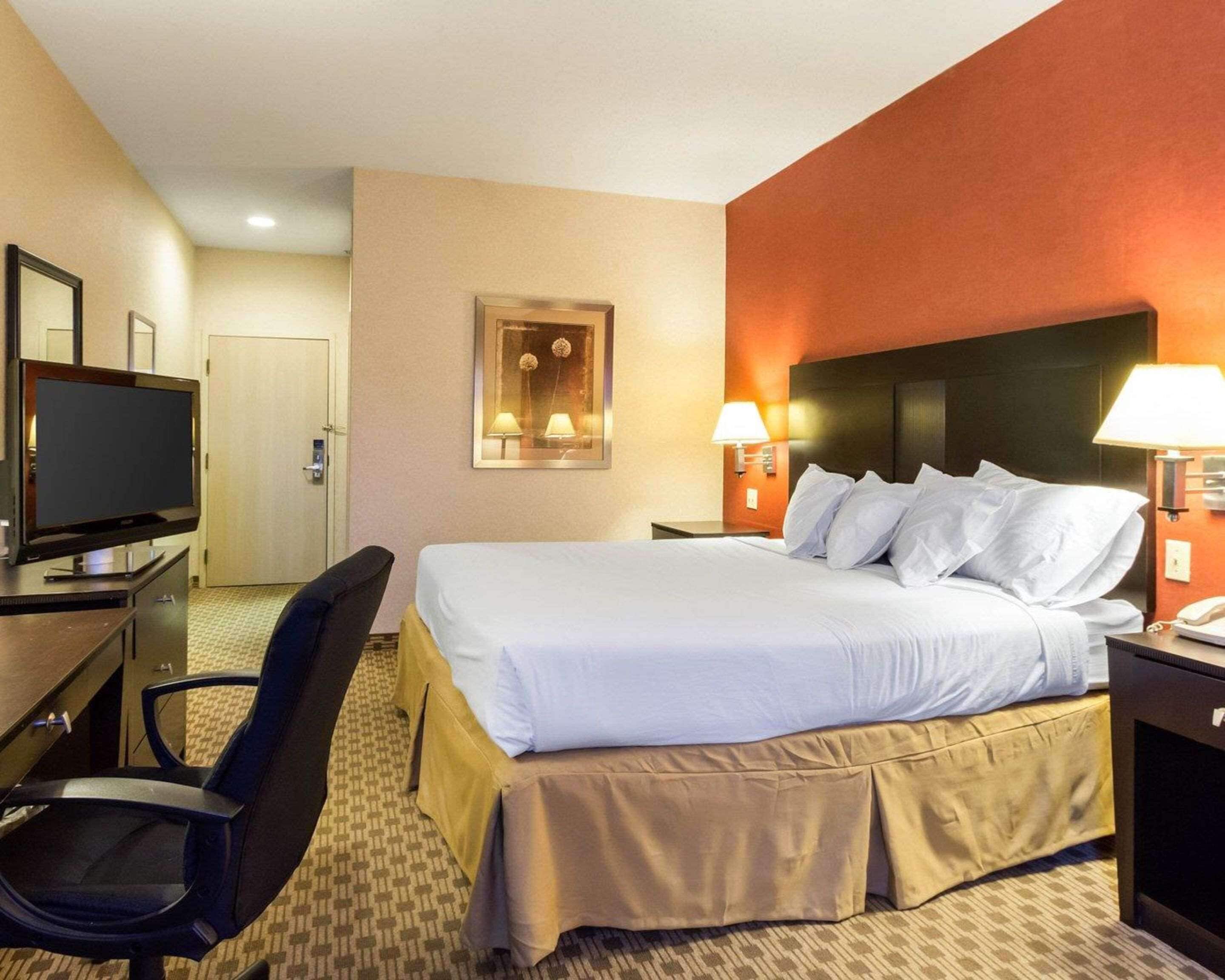 A hotel room with a bed, a desk with a television, a chair, and two bedside lamps.