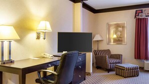 A hotel room with a desk, chair, television, and a sofa with an ottoman.