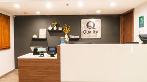 A hotel reception desk with a 'Quality by Choice Hotels' sign, a digital display, a reception counter, and a wall-mounted clock.
