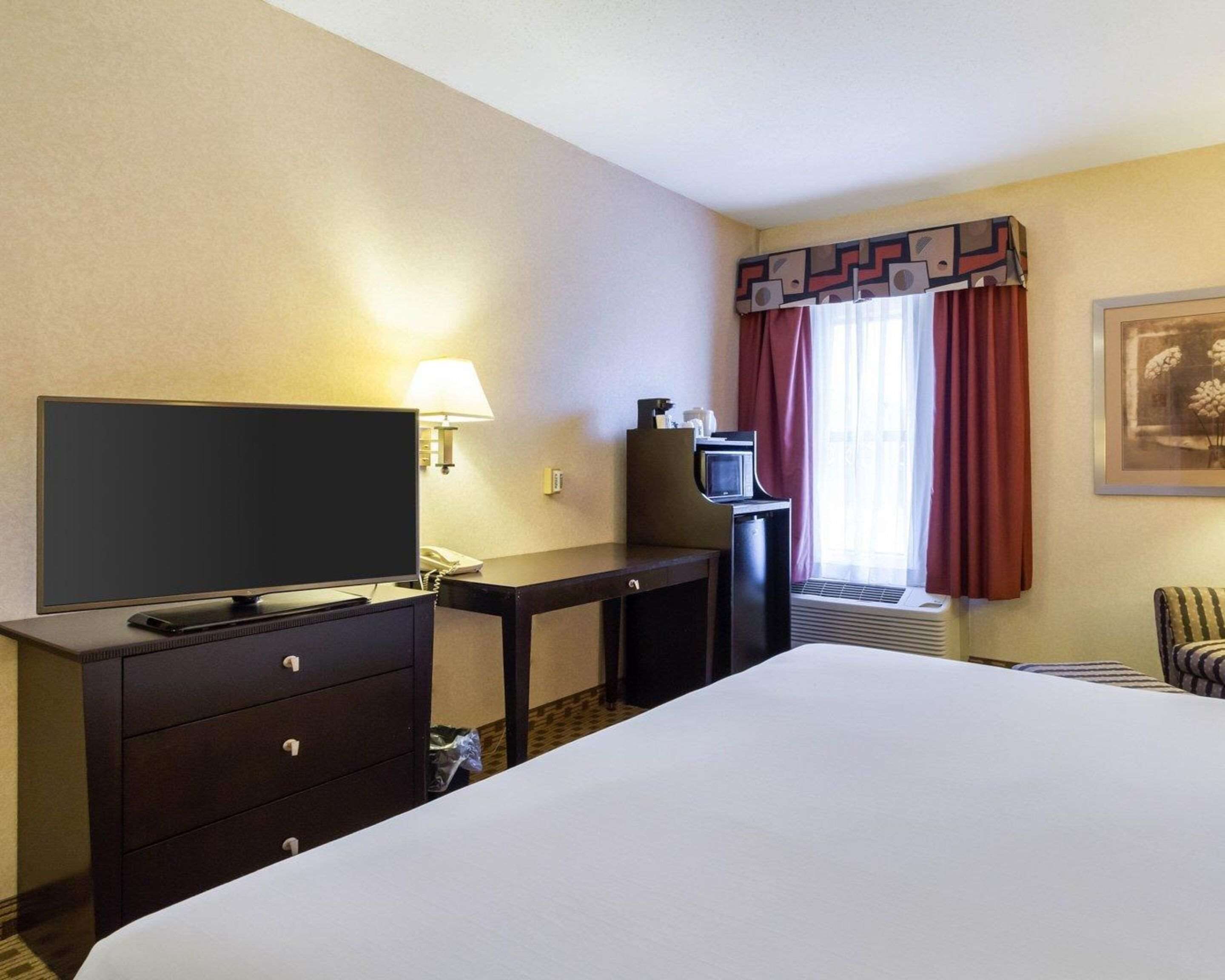 Een hotelkamer met een bed, een bureau met een televisie, een lamp, een magnetron en een stoel.