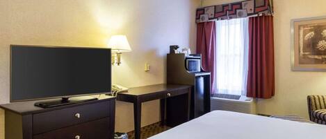 Een hotelkamer met een bed, een bureau met een televisie, een lamp, een magnetron en een stoel.