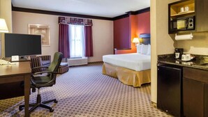 A hotel room with a bed, desk, chair, kitchenette, and a window with curtains.