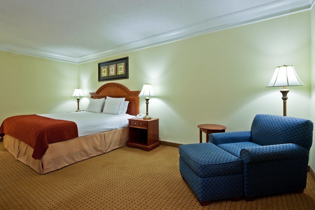 A hotel room with a bed, two bedside tables with lamps, a blue armchair, and a small table.