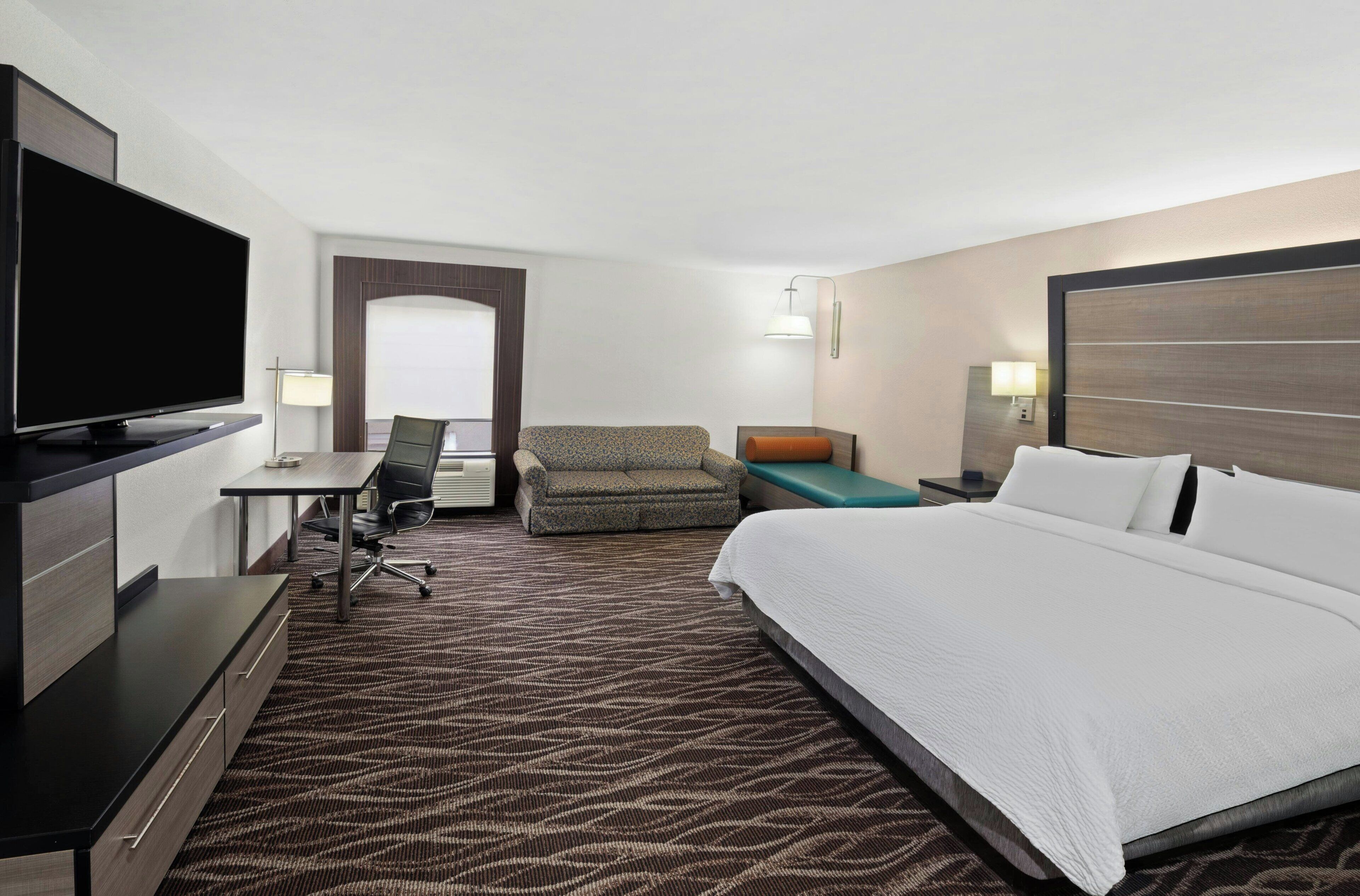A hotel room with a bed, a desk with a chair, a television, and a sofa.
