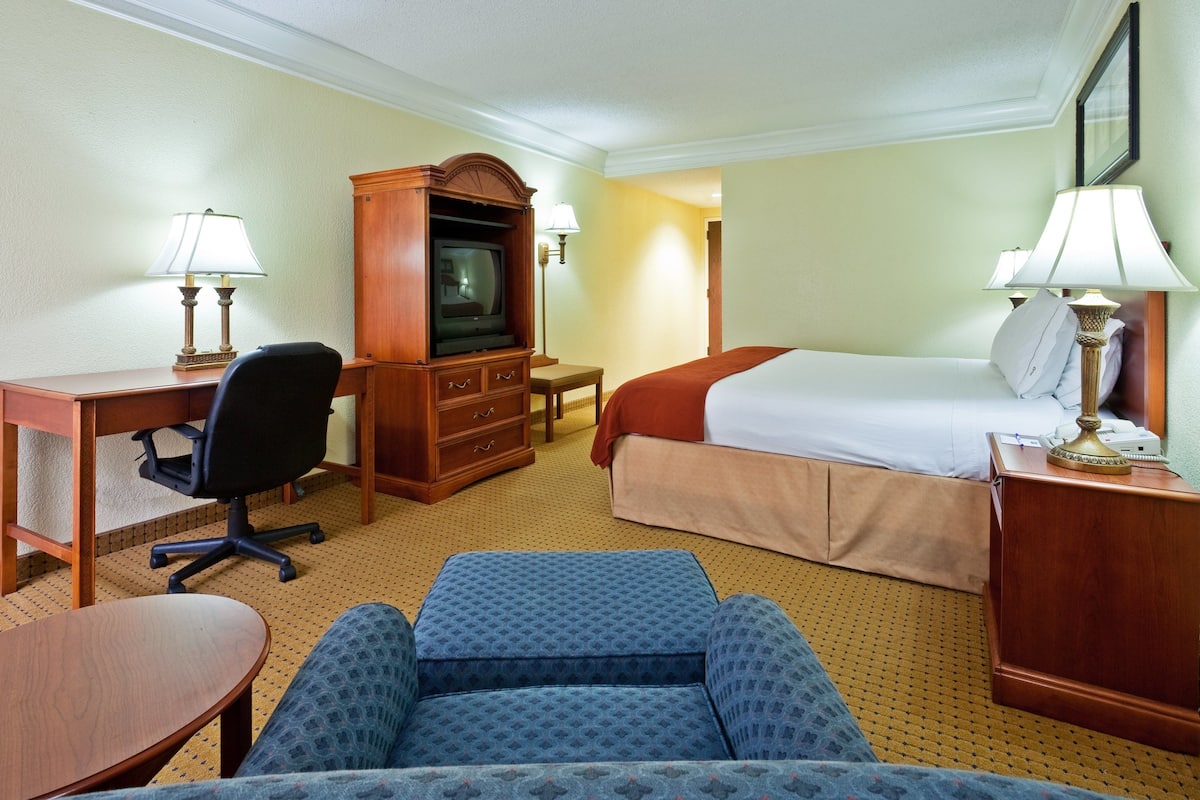 A hotel room with a bed, desk, chair, television, and lamps.