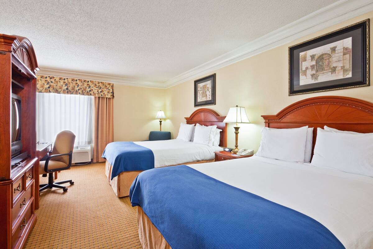 A hotel room with two beds, a desk, a chair, and a television.