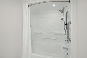 A white shower enclosure with a glass door, a handheld showerhead, a handheld shower attachment, and a handheld shower head.