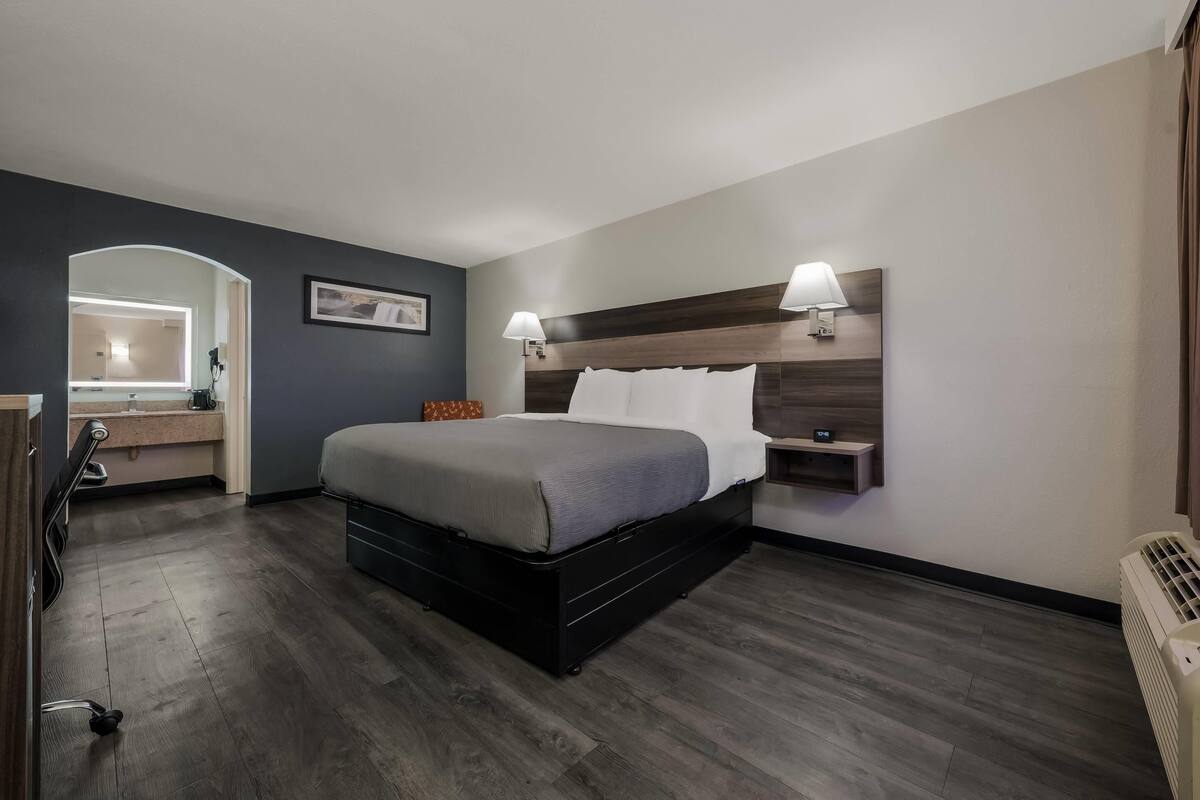 A hotel room with a bed, bedside lamps, a nightstand, a mirror, and a radiator.